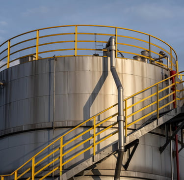 Tanque industrial de almacenamiento plateado con barandales de seguridad amarillos y escaleras metál