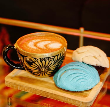Mexican latte in an ornate black and gold cup served with colorful blue and white concha sweet bread.