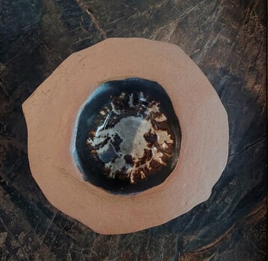 Handmade ceramic clay bowl with a dark glazed center resting on a rustic wood surface.