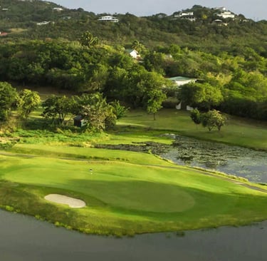A lush tropical golf course green with water hazards, bunkers, and hillside villas in a Caribbean landscape.