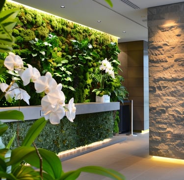 Modern office lobby featuring a lush green moss wall, white orchids, and a textured stone pillar with biophilic design.