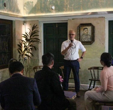A man in a white shirt speaking into a microphone at a public talk event.
