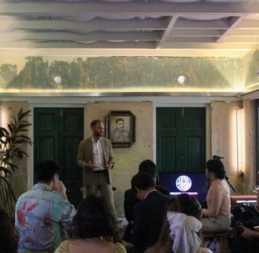 Speaker in a suit leading a business presentation and discussion for an audience in a rustic indoor venue.