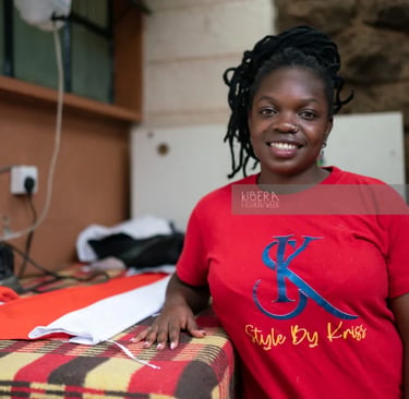 Smiling fashion designer at Kibera Fashion Week posing next to fabrics in a red Style By Kriss t-shirt.