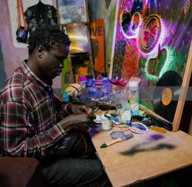 A local artist in a workshop creates handmade jewelry and neon wall art in Kibera.