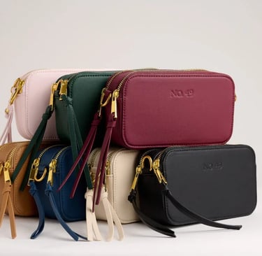 A stack of colorful vegan leather crossbody bags with gold zippers and tassel details for women's fashion.