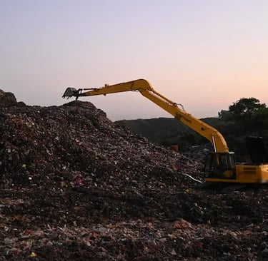 Yellow excavator processing waste at a landfill site during sunset for environmental management.