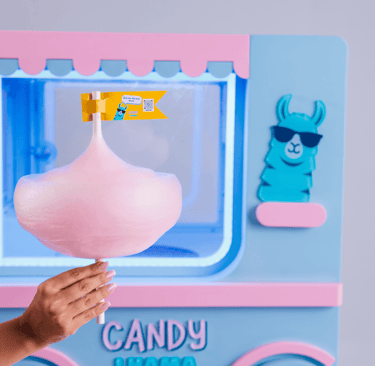 Mão segurando um algodão-doce rosa em frente a uma máquina automática de doces azul