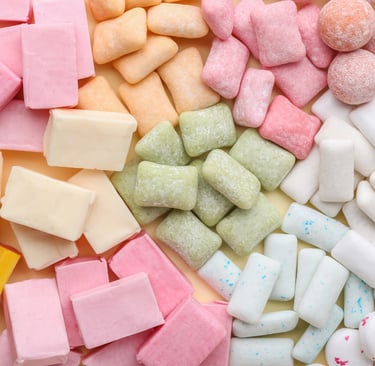 A colorful flat-lay assortment of rectangular and round chewing gum pieces in pink, green, yellow, and white.