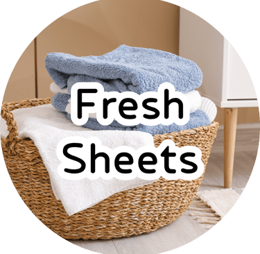 Woven laundry basket with folded blue and white towels and bold overlay text reading "Fresh Sheets." Clean laundry aesthetic.