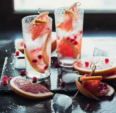 Two tall glasses of sparkling grapefruit drinks with ice, garnished with fresh grapefruit slices and pomegranate seeds.