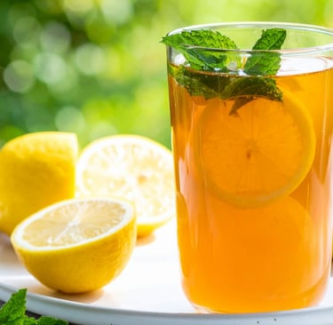A tall, refreshing glass of iced sweet tea with sliced lemons and fresh mint leaves, shot on a sunny afternoon.
