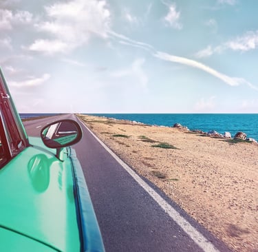 View looking down an open coastal highway and blue ocean from a vintage green car window.