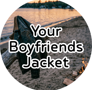 A leather jacket draped over driftwood on a sandy beach at sunset, with a small campfire burning by the water.