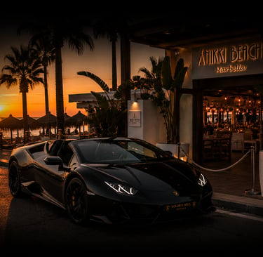 Black Lamborghini luxury car rental parked outside Nikki Beach Marbella at sunset.