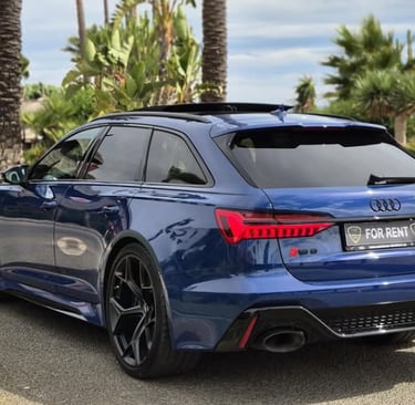 Blue Audi RS6 Avant luxury rental car parked on a tropical coastal road with palm trees.