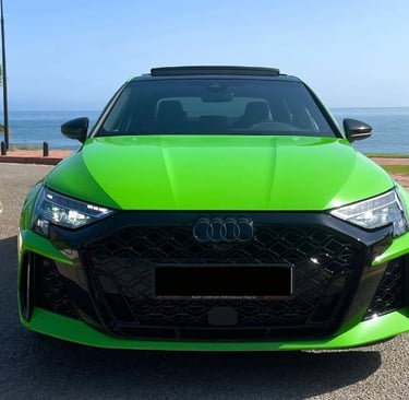 Front view of a bright green Audi RS3 parked on a coastal road with an ocean background.