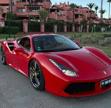 Red Ferrari 488 luxury sports car for rent parked on a street near Mediterranean villas.