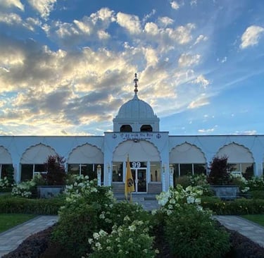 White Sikh Gurdwara temple with domed architecture and garden at sunset