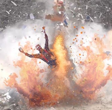 Hank in a red flannel shirt thrown by a large cinematic fire explosion with debris in the air.