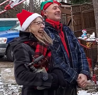 Hank & Stells wearing Christmas hats celebrates outdoors in a snowy yard with holiday decorations.