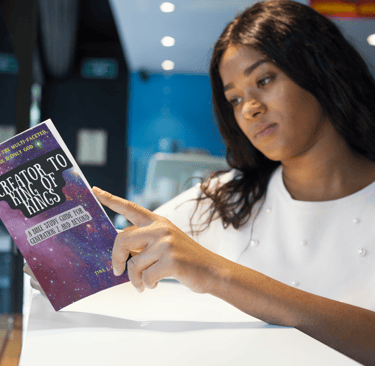 A teenage, black girl reading a book titled Creator To King of Kings.
