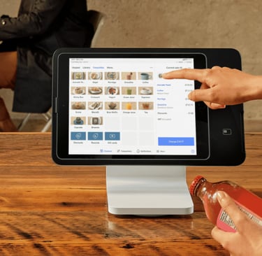 A person uses a digital tablet POS system on a wooden counter to process a retail transaction.