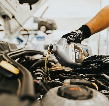 Professional mechanic pouring fresh synthetic engine oil into a car during a routine oil change service.
