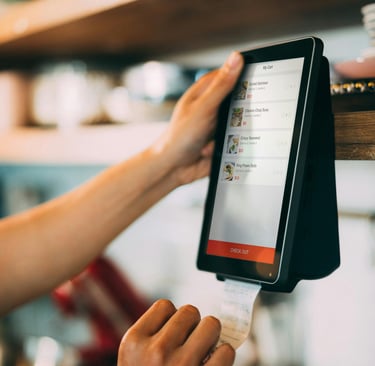 A person using a digital tablet POS system to checkout a food order in a modern cafe.