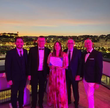Professional group holding an award certificate on a balcony overlooking a sunset cityscape.