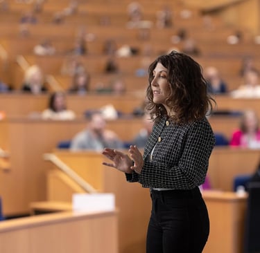 A woman in business attires speaks to an audience in a lecture hall.