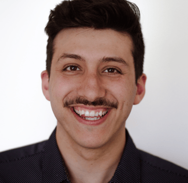 Smiling man with dark hair and mustache against a plain white background, wearing a dark shirt. 