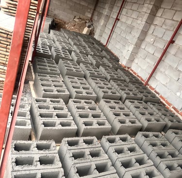 Rows of grey concrete hollow blocks stored in a warehouse for building and construction projects.