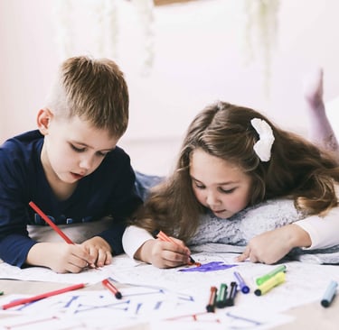 A girl and a boy are colouring in a colouring book whilst lying on the floor