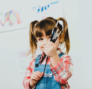 A happy girl standing with paint brushes hands.