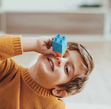 Smiling child holding a block to their eye.
