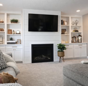 Modern living room with white built-ins, wall-mounted TV above fireplace, neutral decor, gray sofa.