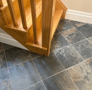 Natural oak wood staircase landing on a grey slate tile floor.