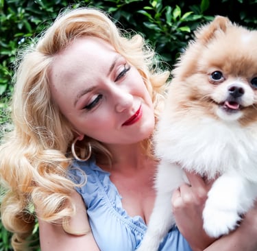 Founder of Liebe Chronicles holding Liebe, a dapper toy pomeranian, in a lush garden setting