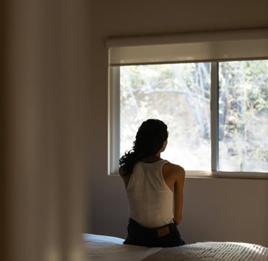 /a-woman-sitting-on-a-bed-looking-out-a-window