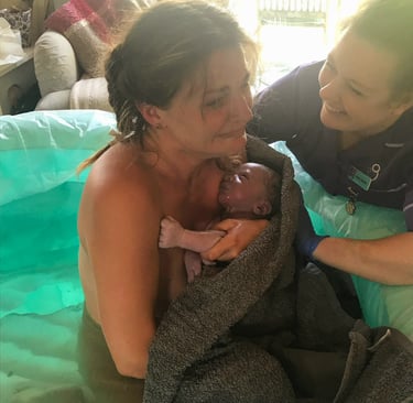A mother holding her newborn baby after a successful waterbirth with the support of a midwife.