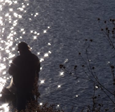 a shadow of a man standing in front of a sparkling lake