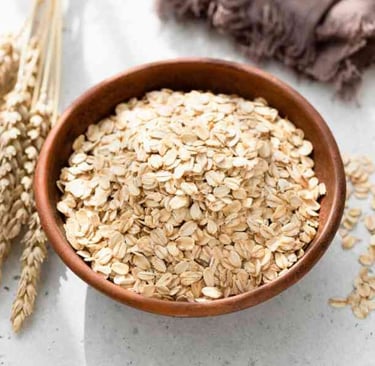A wooden bowl of oats with oat sheafs next to it