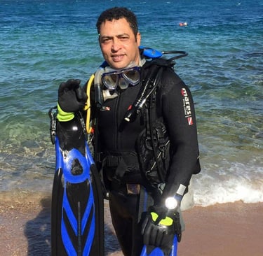 Captain Essam in a wetsuit and scuba gear standing in front of a body of