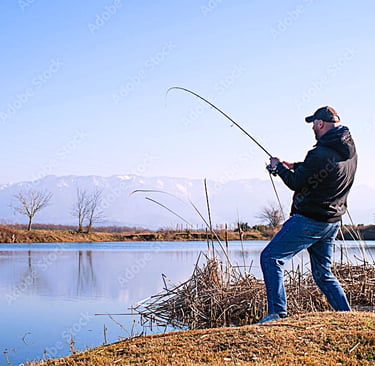 homem com jaqueta preta pescando em pé a beira do lago pisando em capim seco