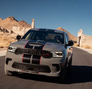 A grey Dodge Durango SRT Hellcat with racing stripes driving past desert ruins.
