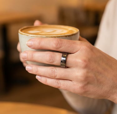 a woman holding a cup of coffee in a cafe and wearing an oura ring