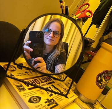 Woman with glasses taking a mirror selfie on a desk with books and office supplies.