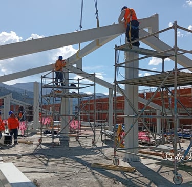 Construction workers in safety gear install steel beams and scaffolding at an industrial building site.
