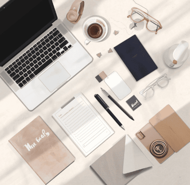 Flat lay of a modern workspace with laptop, coffee, notebooks, and pens on a bright desk.